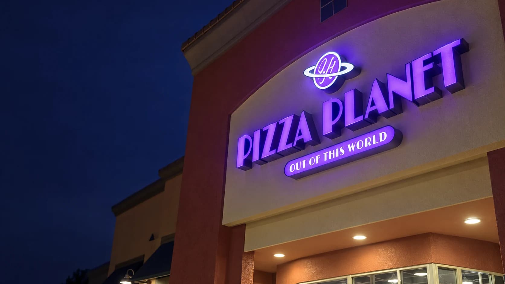 Purple illuminated Pizza Planet channel letters on a storefront at night